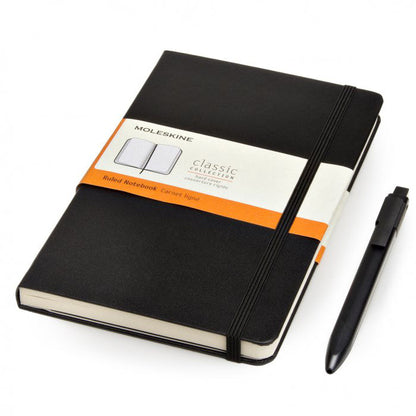 Black Moleskine ruled hard-cover notebook with elastic closure and black click pen alongside