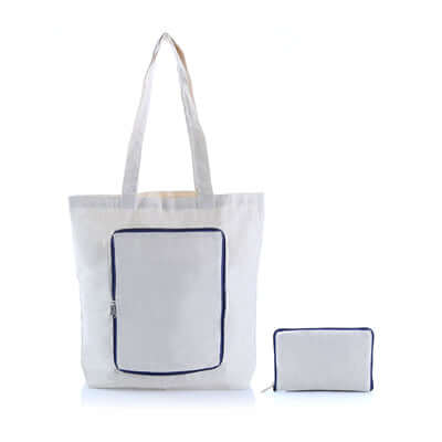 Light-coloured canvas zipper foldable tote with a dark-blue-trimmed front panel, shown beside its folded rectangular pouch