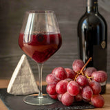 Luigi Bormioli Atelier 610ml Wine Glass filled with red wine next to grapes and a wine bottle.