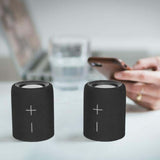 Prixton Aloha Lite Bluetooth Speaker in a stylish black design on a table with a smartphone.
