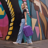 Woman walking with Cabinzero Classic Backpack 28L in vibrant purple against a colorful mural.