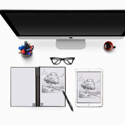 Open Rocketbook notebook with a tree sketch beside a tablet displaying the same drawing in an illustrative desk scene
